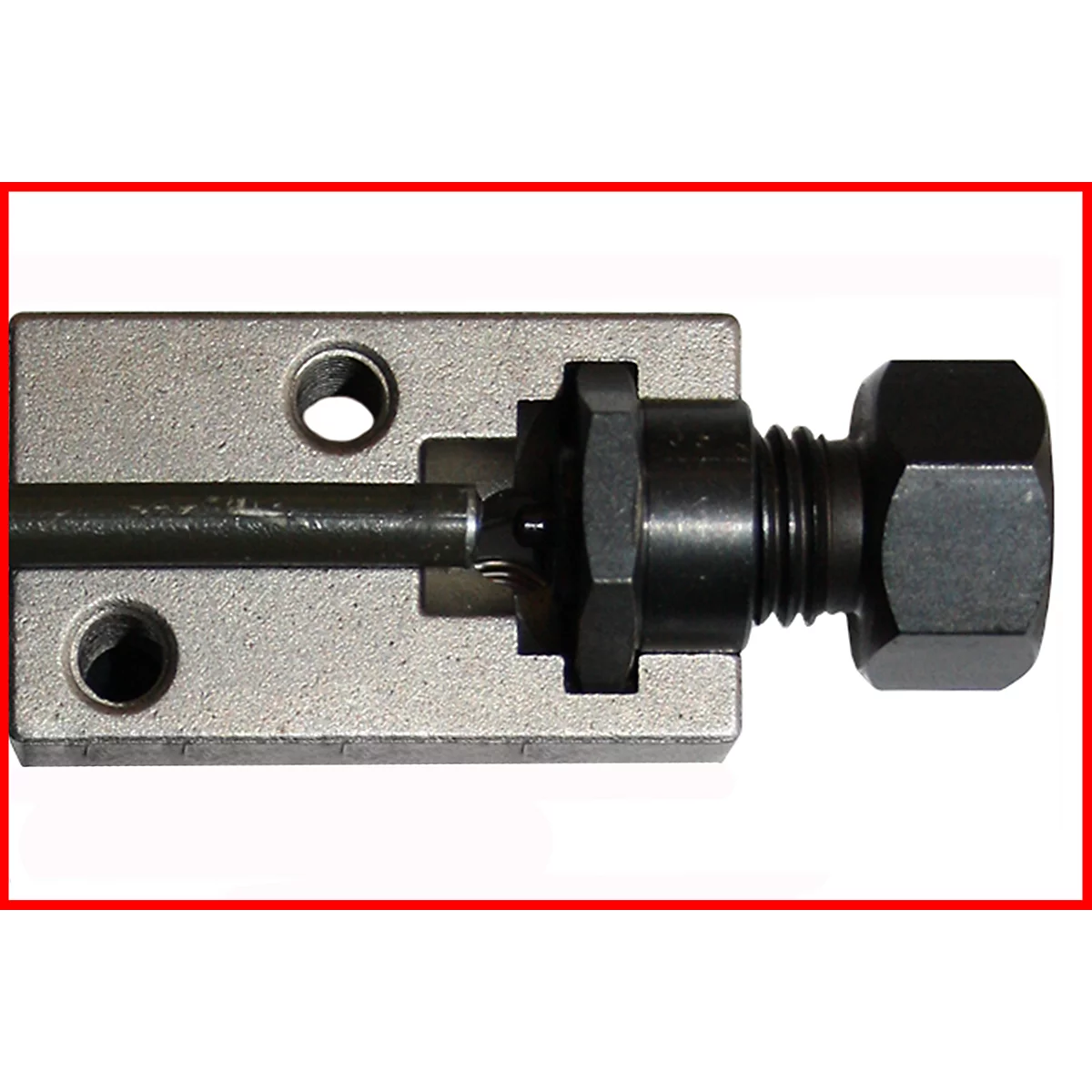 Nahaufnahme eines Metallwerkzeugs, das aus einem silbernen Block, einer Schraube, einer schwarzen Mutter und einem Stab besteht.